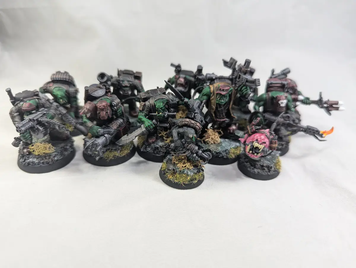 A collection of painted green orc miniatures from the Warhammer 40,000 universe, each armed with various weapons and…