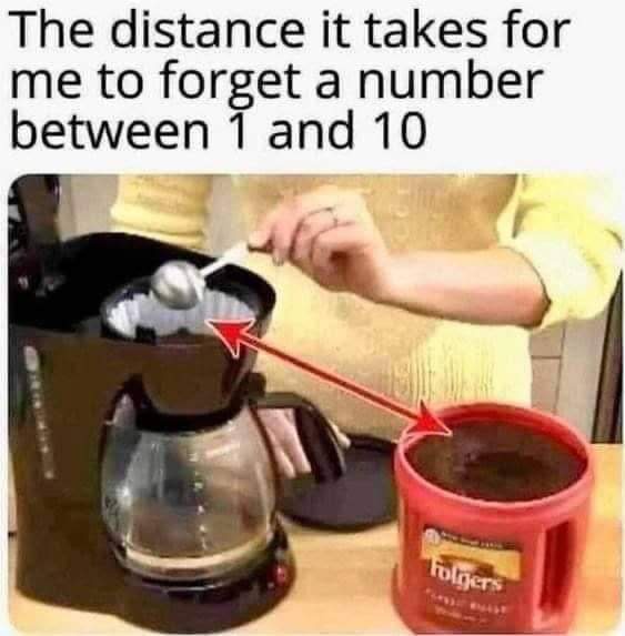 A person in a yellow sweater uses a spoon to scoop coffee grounds from a red Folgers container into a coffee maker. Two red…