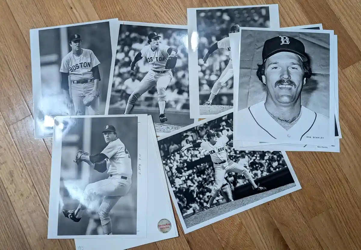 Several black-and-white photographs of baseball player Bob Stanley in Boston Red Sox uniforms are spread out on a wooden…