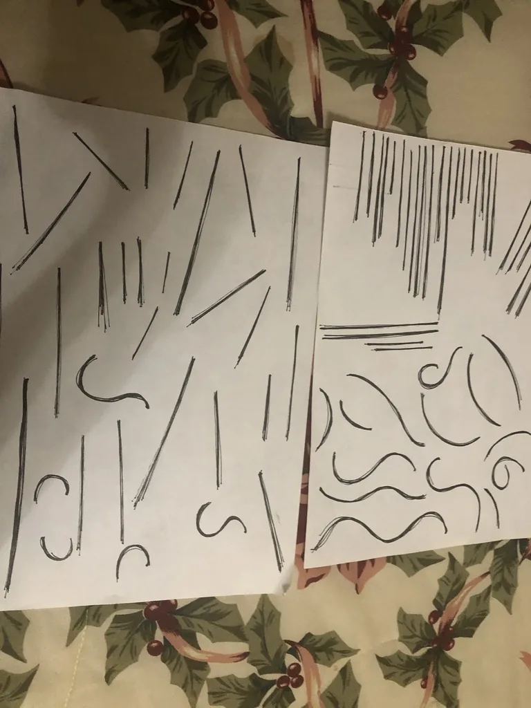 Two sheets of paper with messy, abstract scribbles and lines are laid on a holly-patterned fabric. The left sheet has mostly…