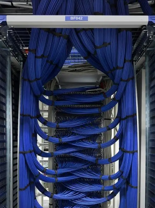 A close-up photo of a server rack with neatly bundled blue Ethernet cables cascading down like curtains, with a blue label…