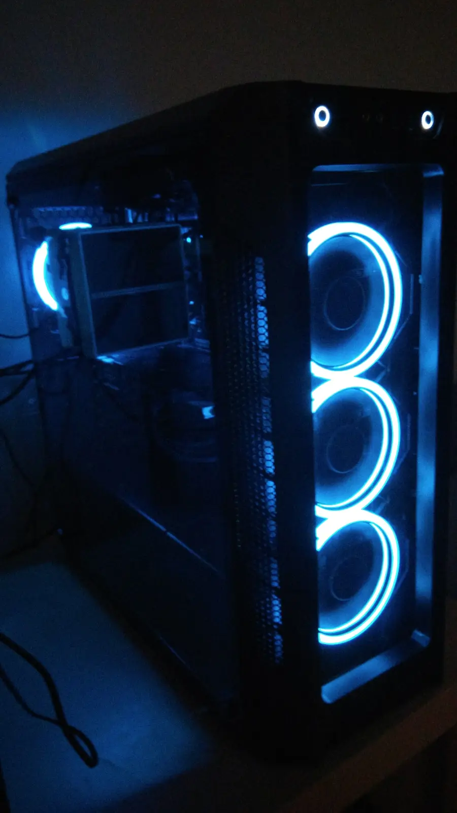 A black computer case with a transparent side panel is shown in a dim room, illuminated by bright blue LED lights around…