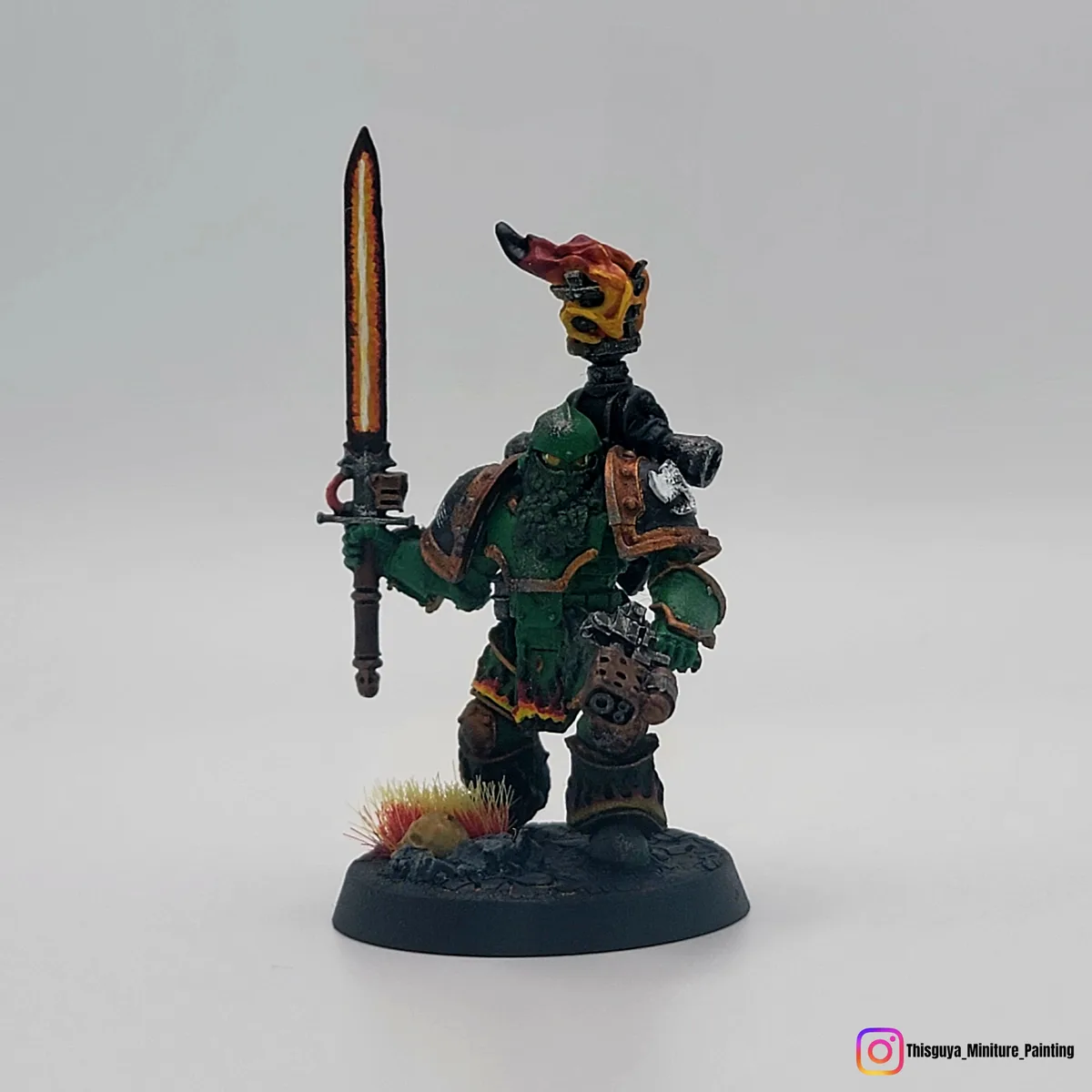 A painted miniature of a green-skinned, armored warrior with a flaming skull on his shoulder, holding a glowing sword…