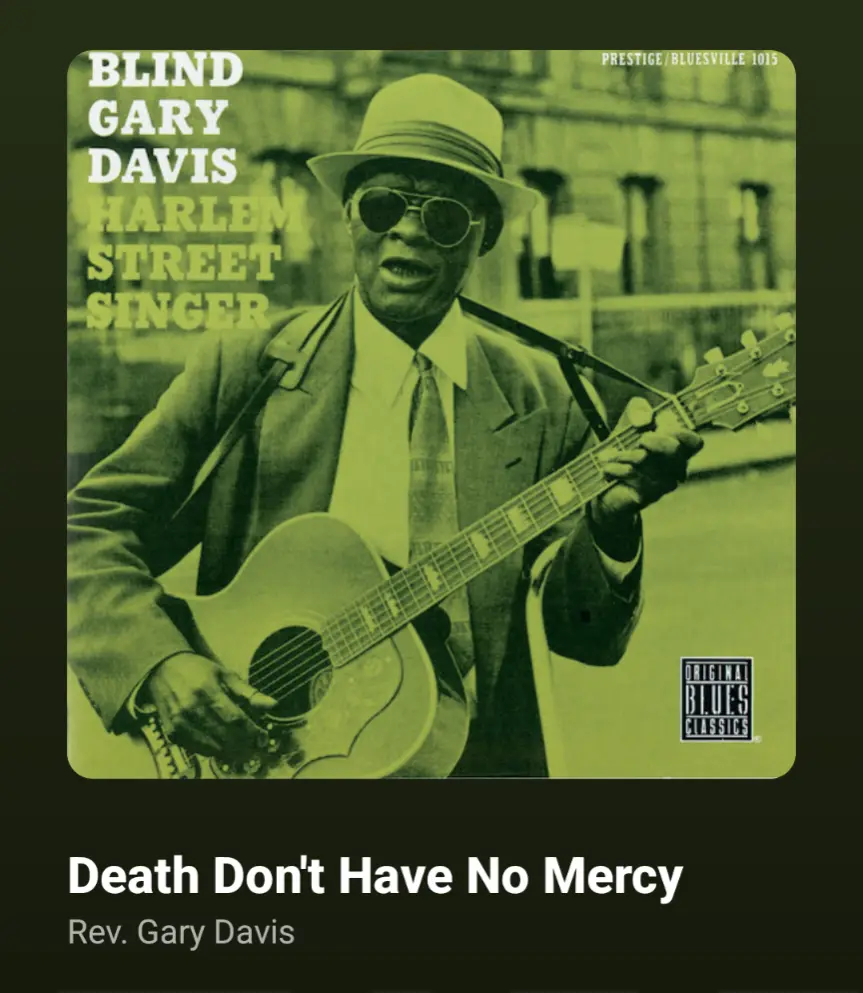 The image is a vintage album cover featuring a Black man in a suit, hat, and sunglasses, playing an acoustic guitar while…