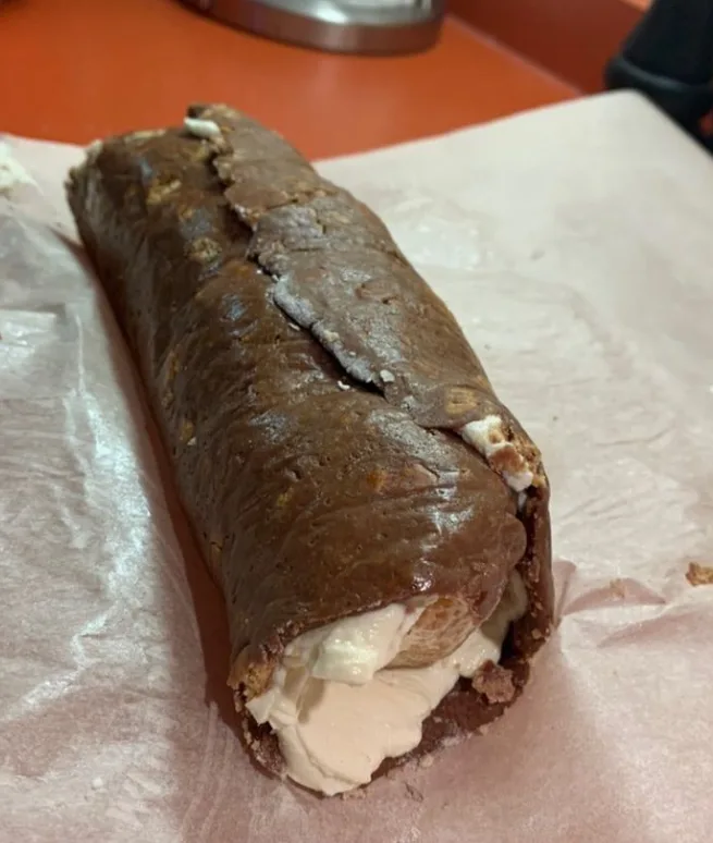 a close-up photo of a chocolate roll cake with a creamy white filling, resting on crinkled parchment paper. The cake's…