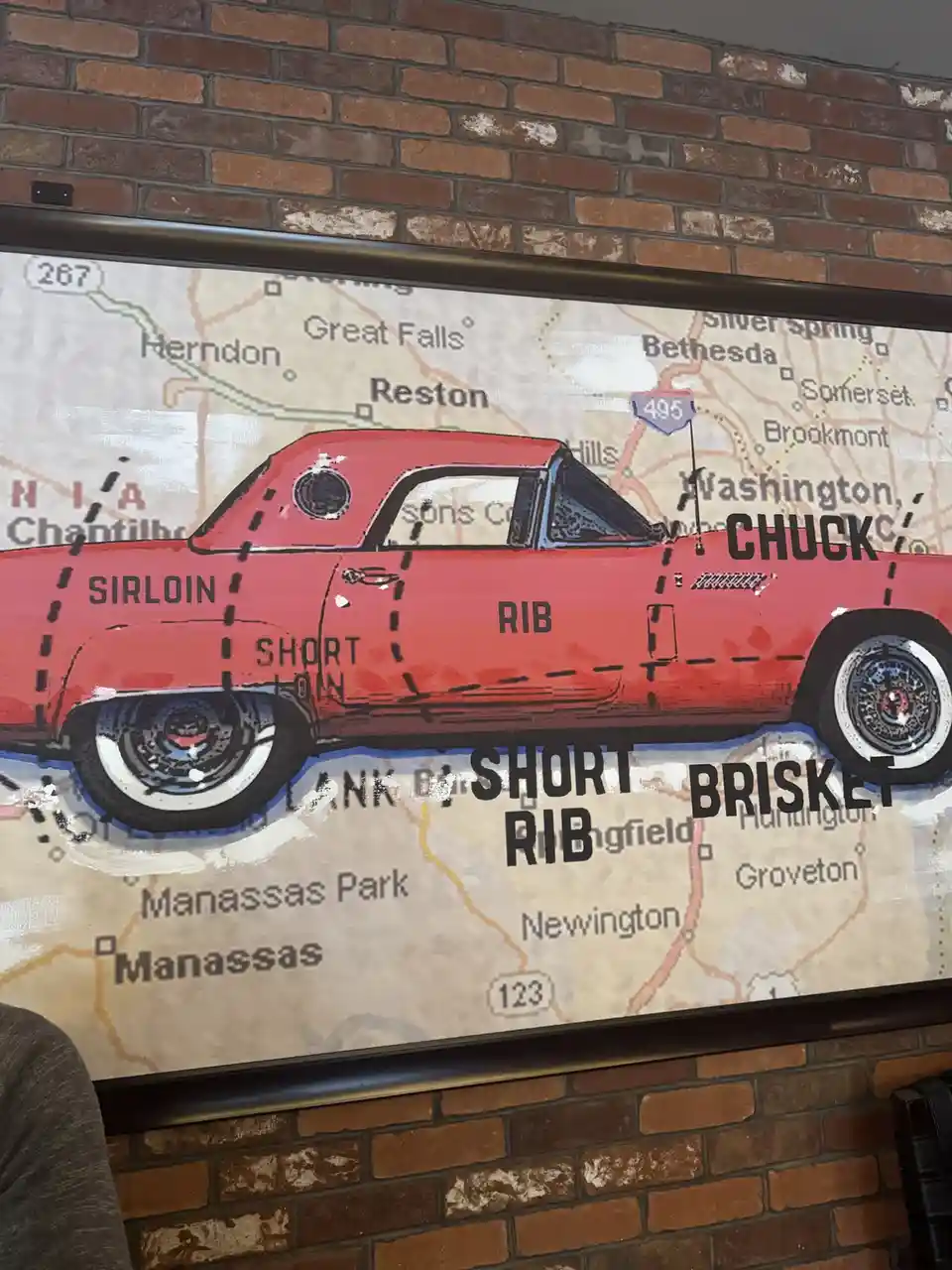 A red vintage car is painted on a wall mural over a map of the Washington D.C. area, with cuts of beef like 'SIRLOIN'…