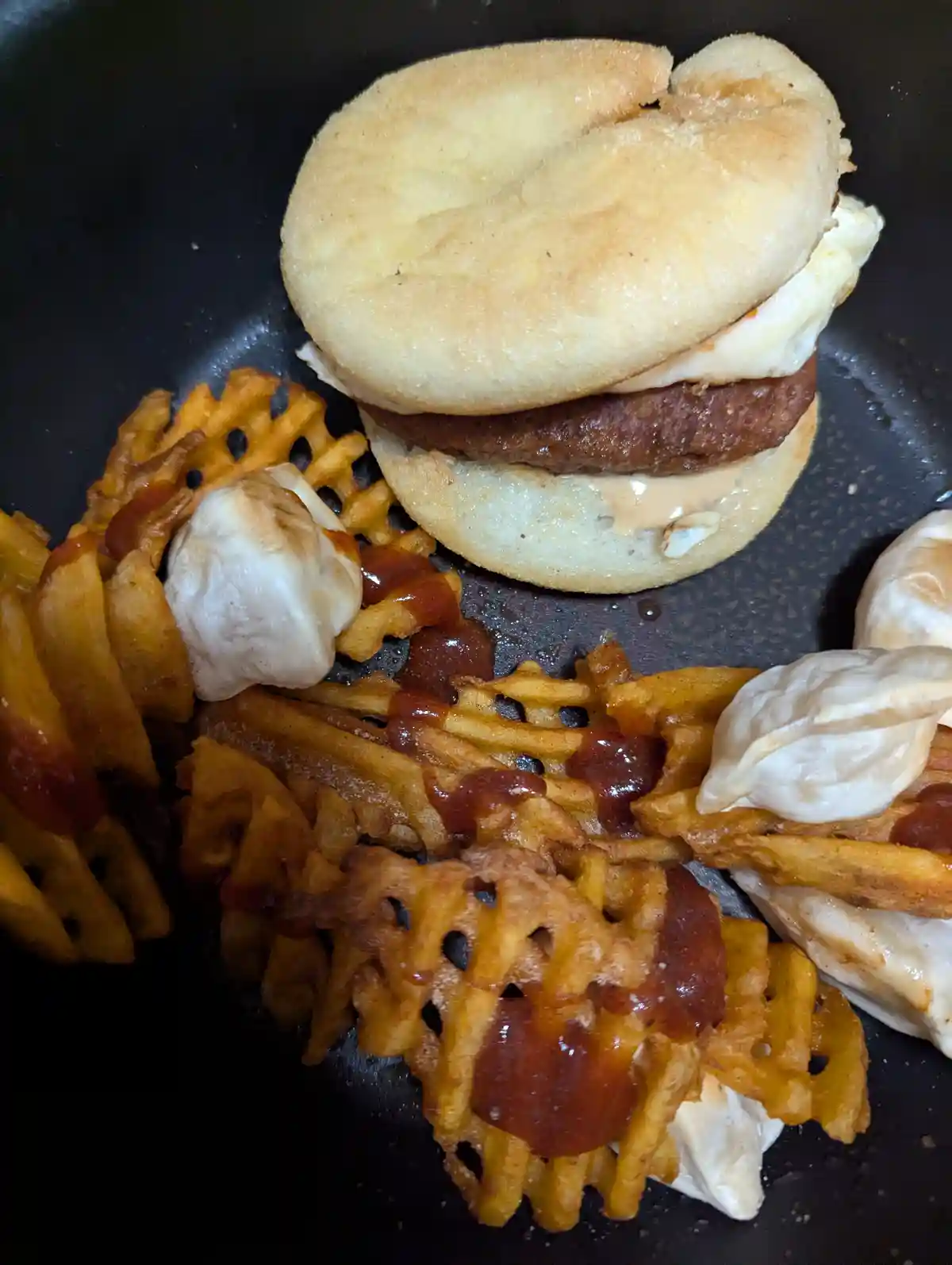A close-up photo shows a burger in a toasted bun with a patty and melted cheese, sitting next to waffle fries topped with…