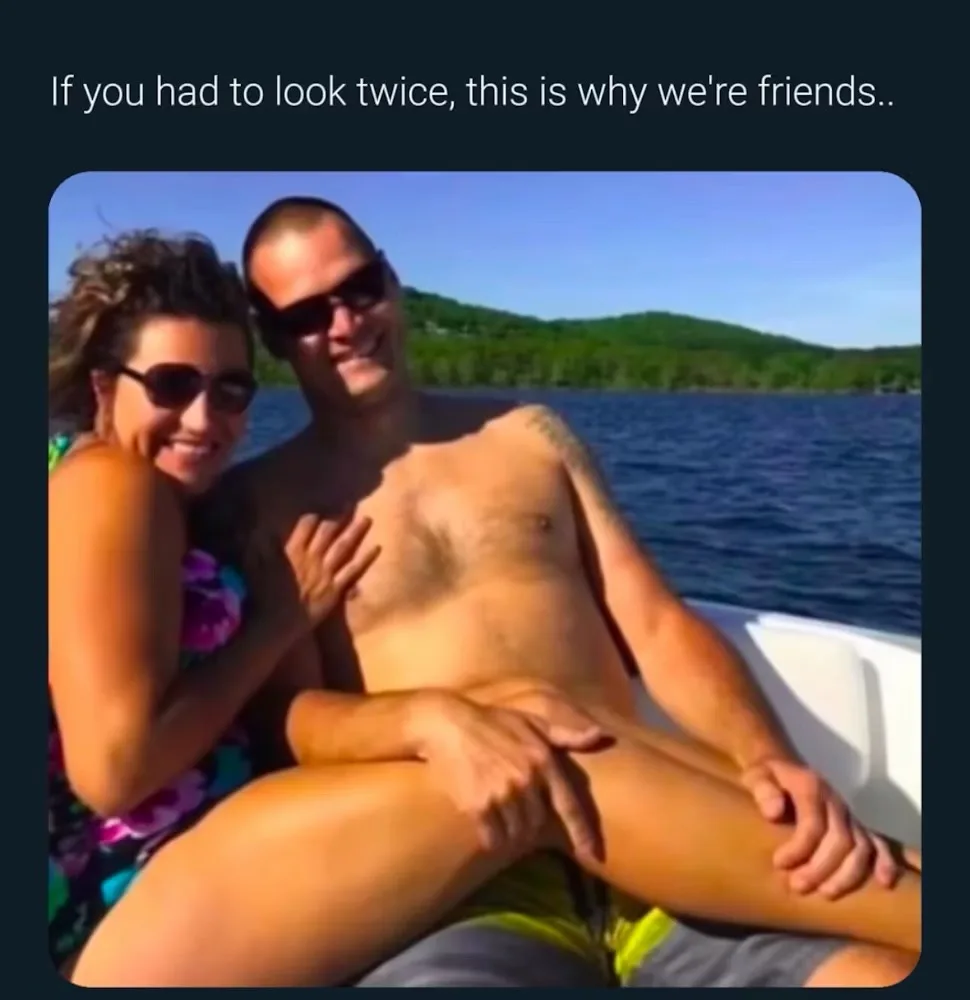 A shirtless man and a woman in sunglasses are posing together on a boat, with the woman's leg draped over the man's lap. The…