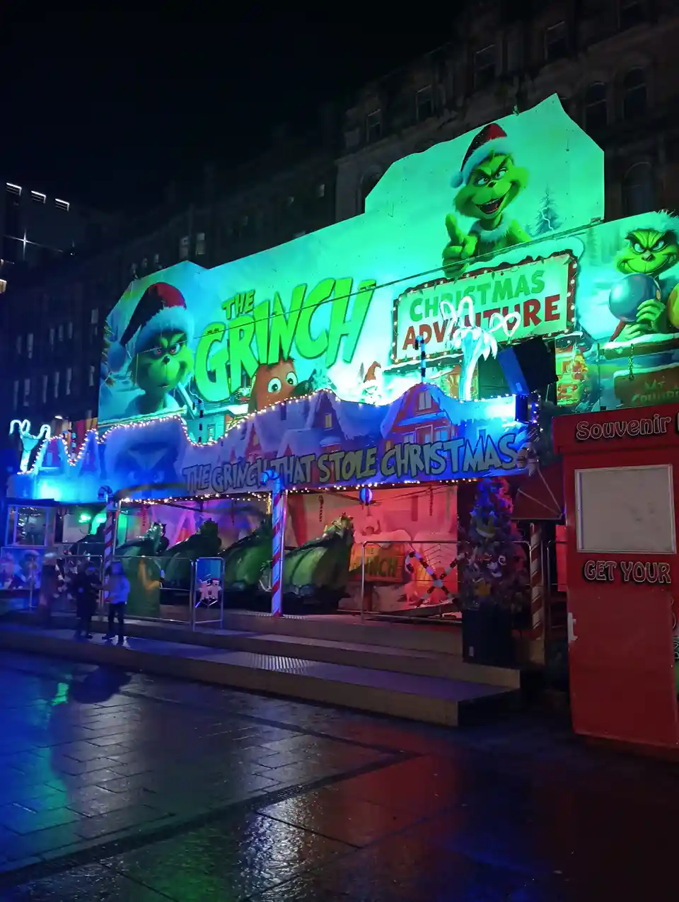 A brightly lit, nighttime outdoor attraction for 'The Grinch That Stole Christmas' features large green Grinch characters…