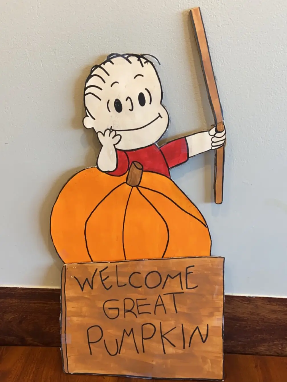 A handcrafted wooden cutout of the cartoon character Charlie Brown, wearing a red shirt and sitting atop a large orange…