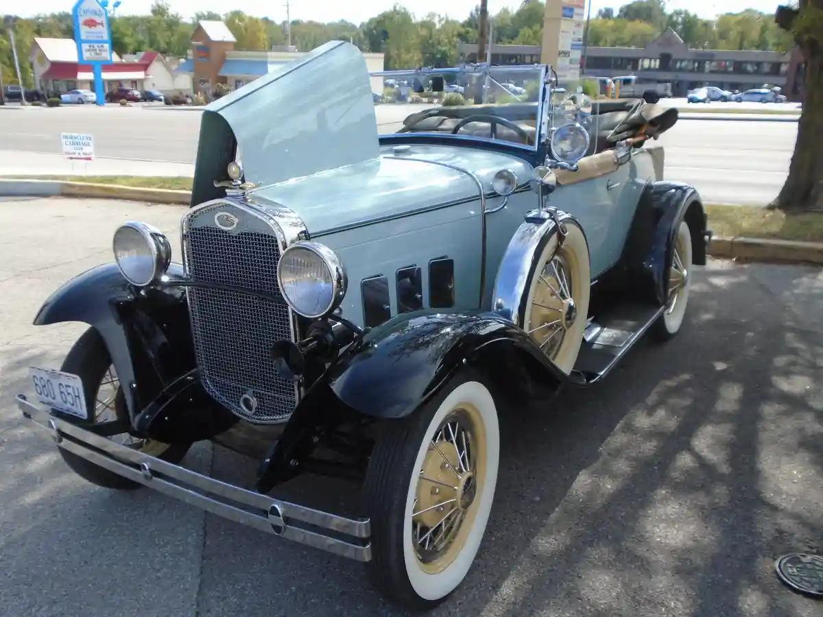 A vintage light blue and black Ford Model A convertible with whitewall tires and chrome accents is parked in a modern…