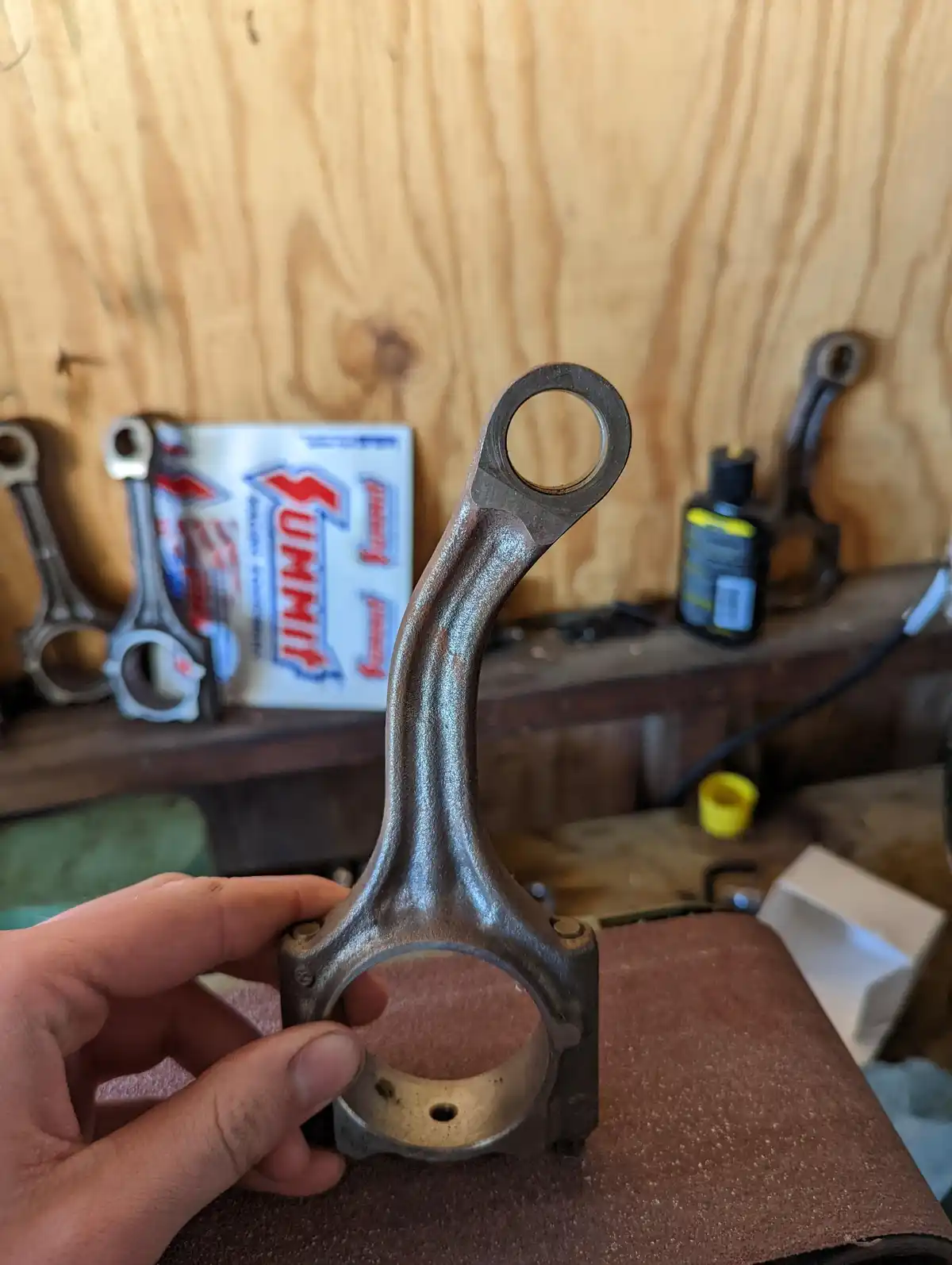 A hand holds a metal connecting rod in a workshop, with other rods and a 'Summit' box visible in the background. The…