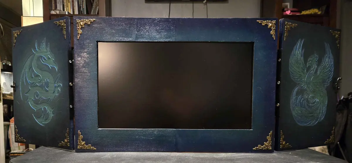 A custom-made, ornate dark blue frame with gold corner embellishments is shown open, revealing a blank black monitor screen…