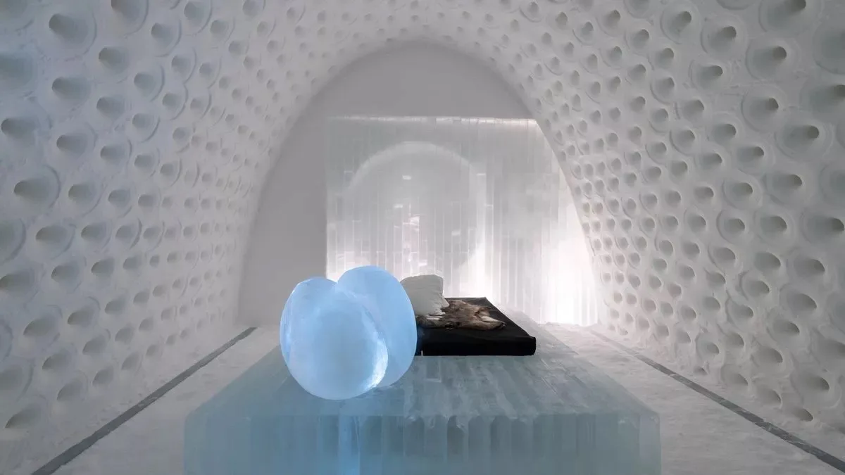 A serene, minimalist ice room with curved, bubble-textured white walls and a translucent ice bed. On the bed are two glowing…