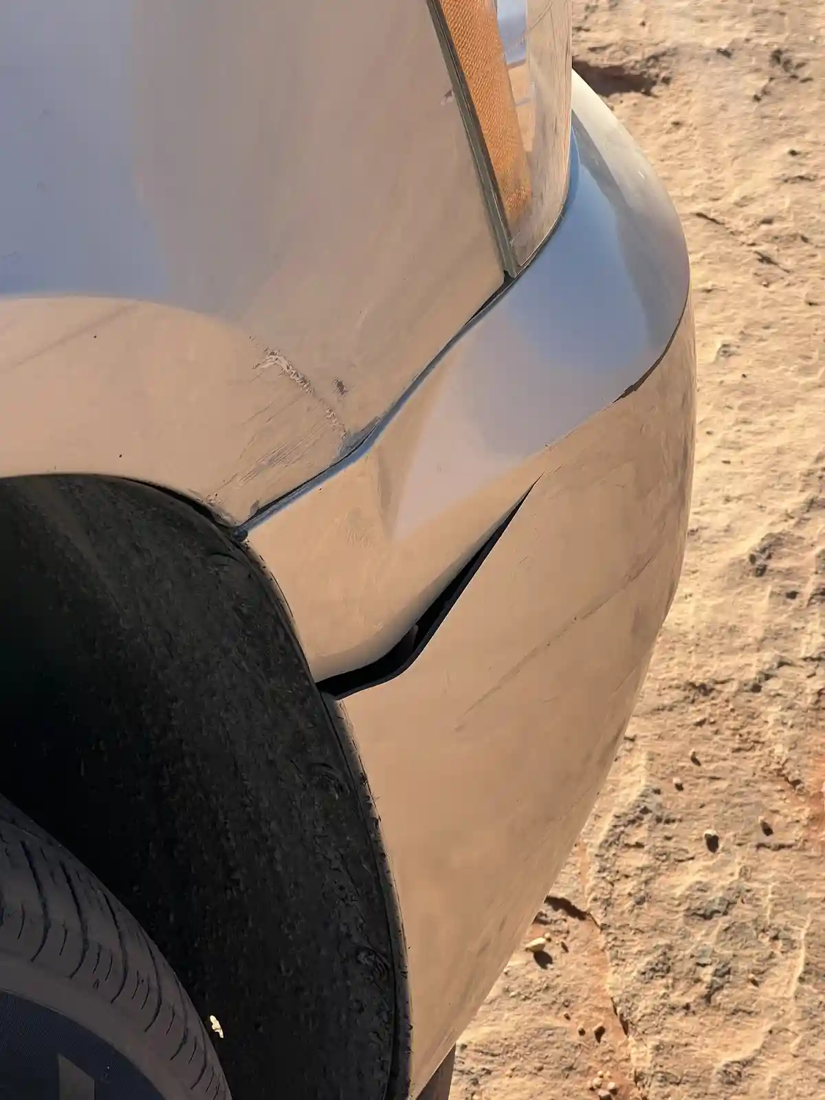 A close-up photo shows the rear quarter panel of a light-colored car with visible damage, including a deep crack and scuff…