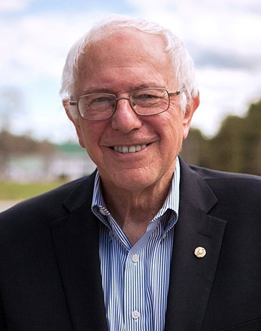 A smiling portrait of Bernie Sanders, an older man with white hair and glasses, wearing a dark suit jacket over a blue and…