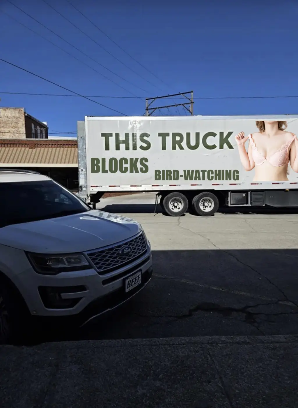 A large white semi-truck with a billboard on its side is parked on a street, partially blocking a silver Ford SUV in the…