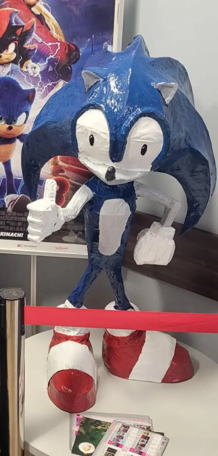 A large, handmade papier-mâché statue of Sonic the Hedgehog, made from blue and white paper mache, stands on a white table…