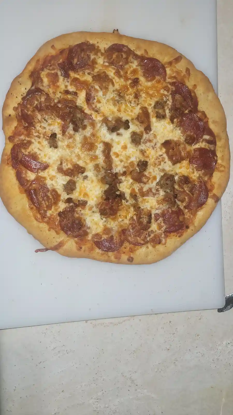 A top-down photo of a pepperoni and sausage pizza on a white cutting board, with the text 'this is not a pizza, this is a…
