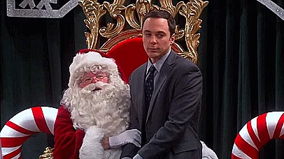 The image shows a split-screen of Sheldon Cooper from The Big Bang Theory sitting next to a Santa Claus figure on a red…