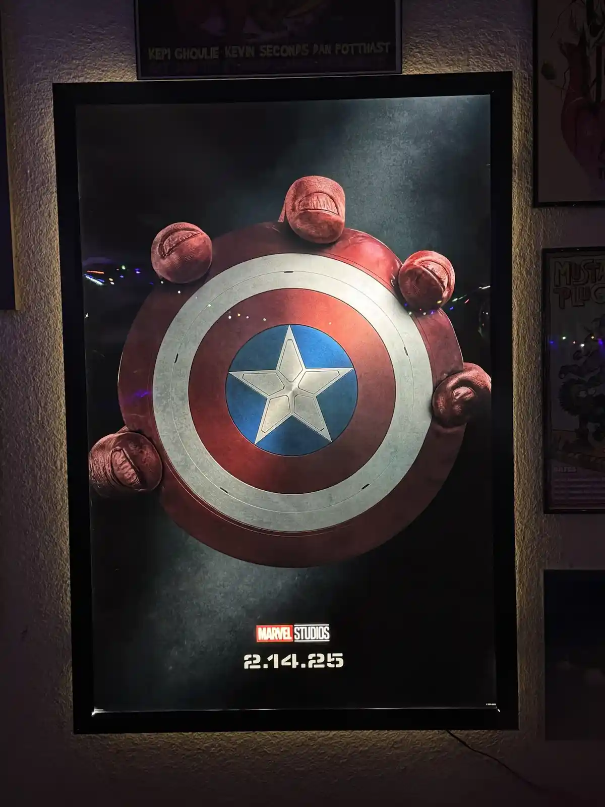 A framed Marvel Studios poster shows Captain America's shield being held by five red, fleshy, worm-like creatures with…