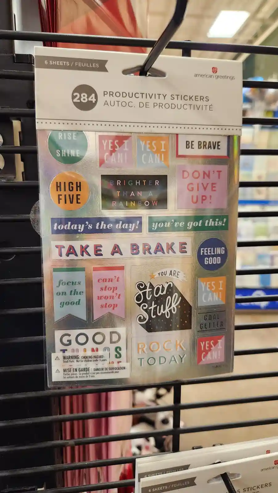 A package of American Greetings 'Productivity Stickers' hangs on a store rack, displaying various motivational phrases like…