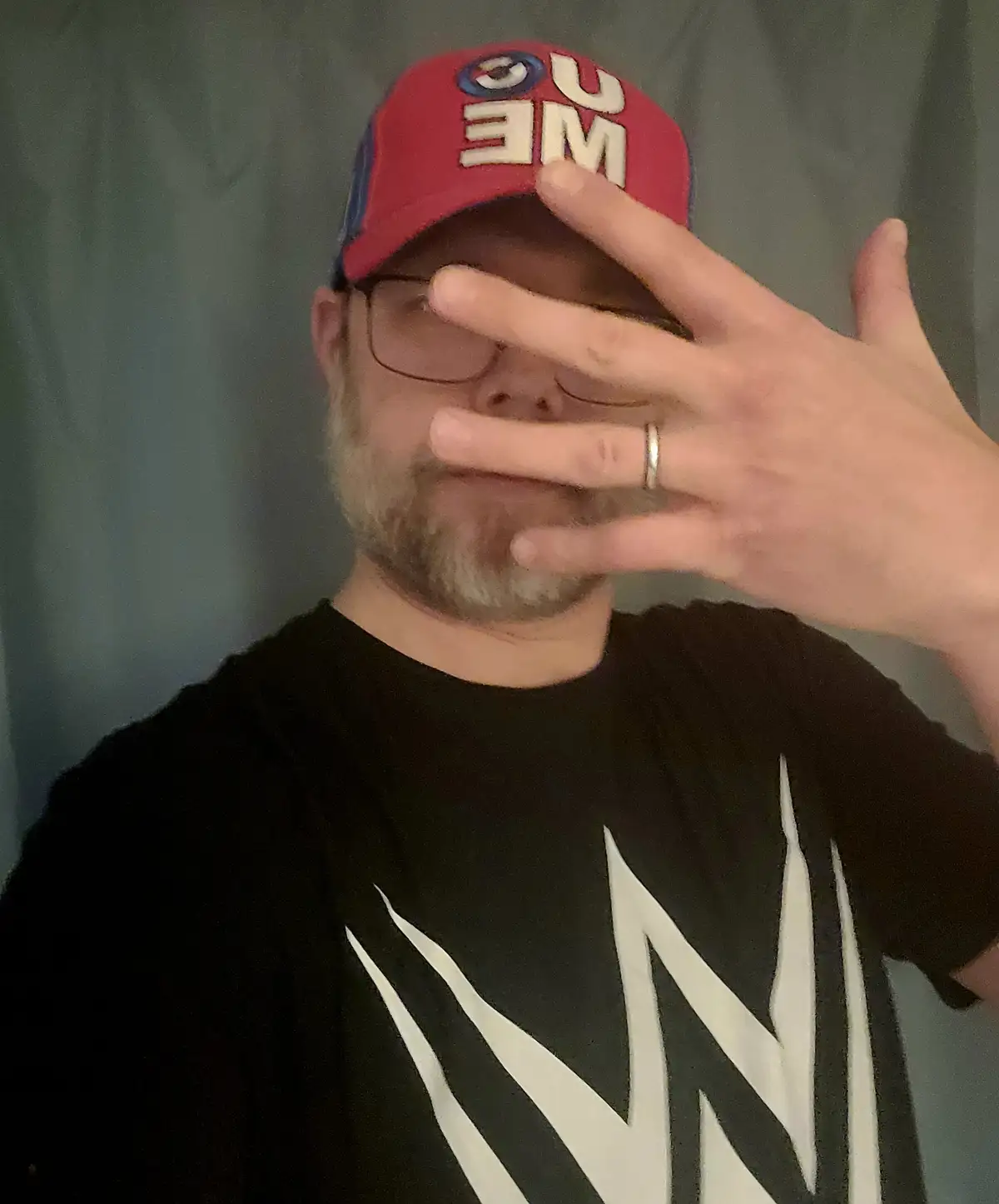A man wearing a red 'SUPREME' baseball cap and glasses holds his hand over his face, obscuring his eyes and mouth, while…