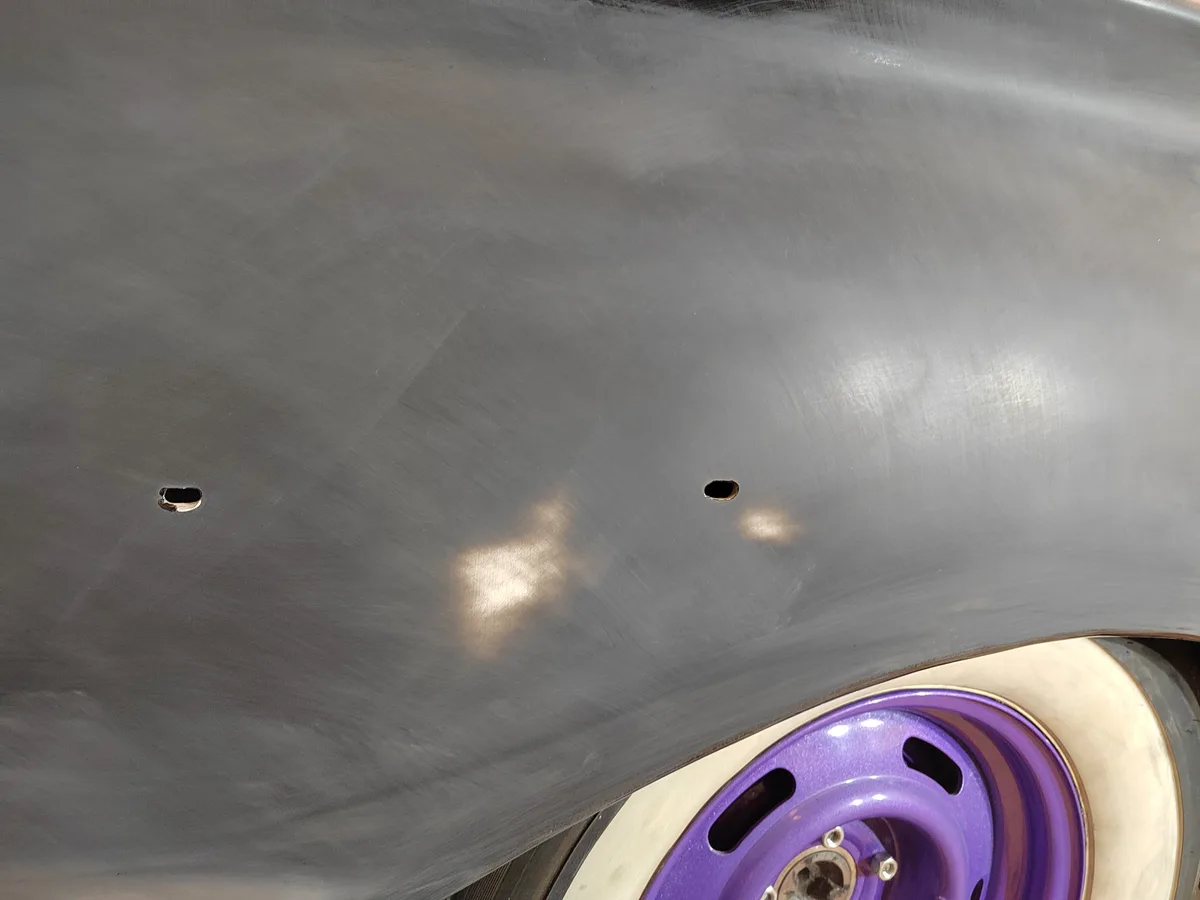 A close-up photo shows the side of a car with a freshly painted gray surface, featuring two small, oval-shaped holes near…