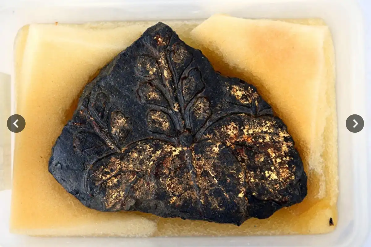 a close-up photo shows a dark, ornately carved object with gold leaf accents, resembling a traditional japanese artifact…