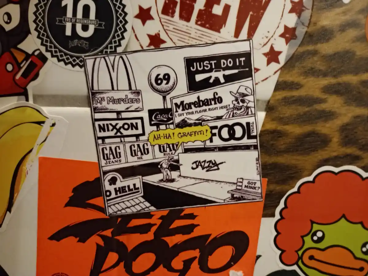 A black-and-white cartoon sticker depicts a police officer pointing at a wall with the word 'JAZZY' spray-painted on it…