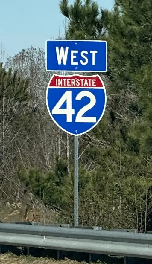 A photo of a U.S. highway sign showing 'WEST' above a blue shield with 'INTERSTATE 42' in white text. The sign is mounted on…