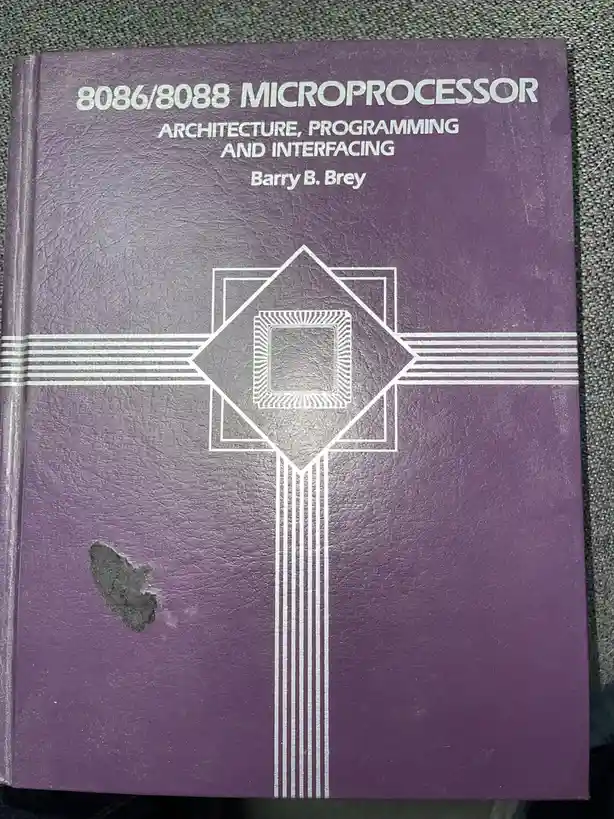 A close-up of a well-worn purple textbook titled '8086/8088 MICROPROCESSOR ARCHITECTURE, PROGRAMMING AND INTERFACING' by…