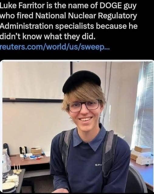 A young man with blonde hair, glasses, and a black beret smiles at the camera while wearing a dark blue polo shirt and a…