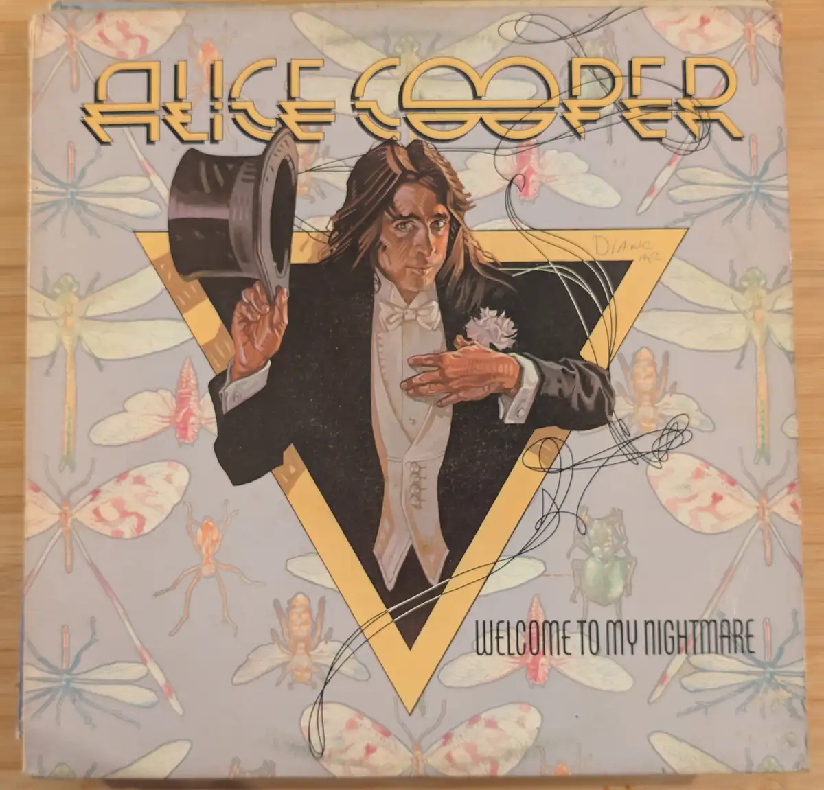 The image shows the iconic album cover for Alice Cooper's 'Welcome to My Nightmare,' featuring a man in a tuxedo holding a…