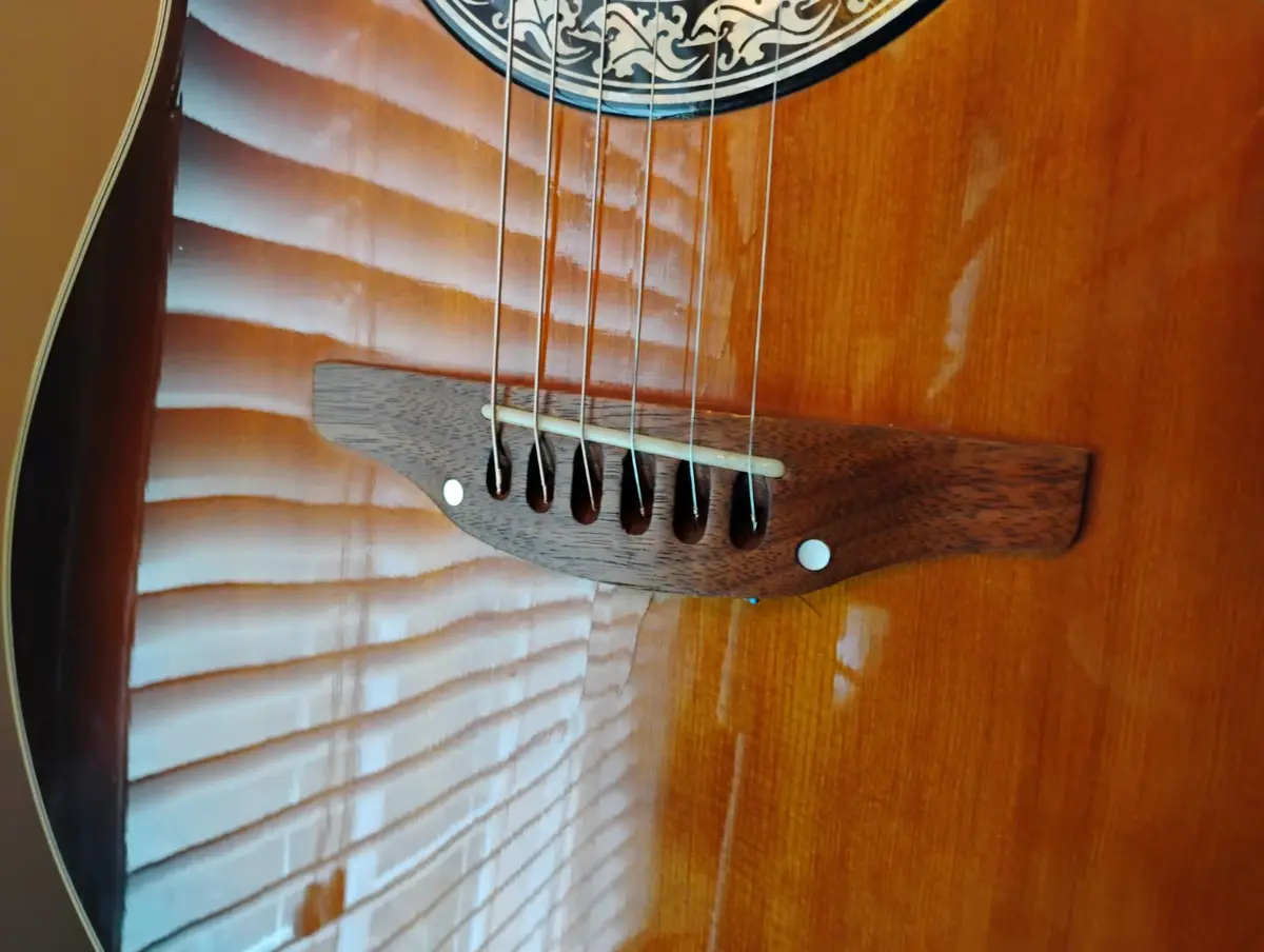 A close-up photo of an acoustic guitar's soundhole and bridge, with light reflecting off the polished wood surface. The…