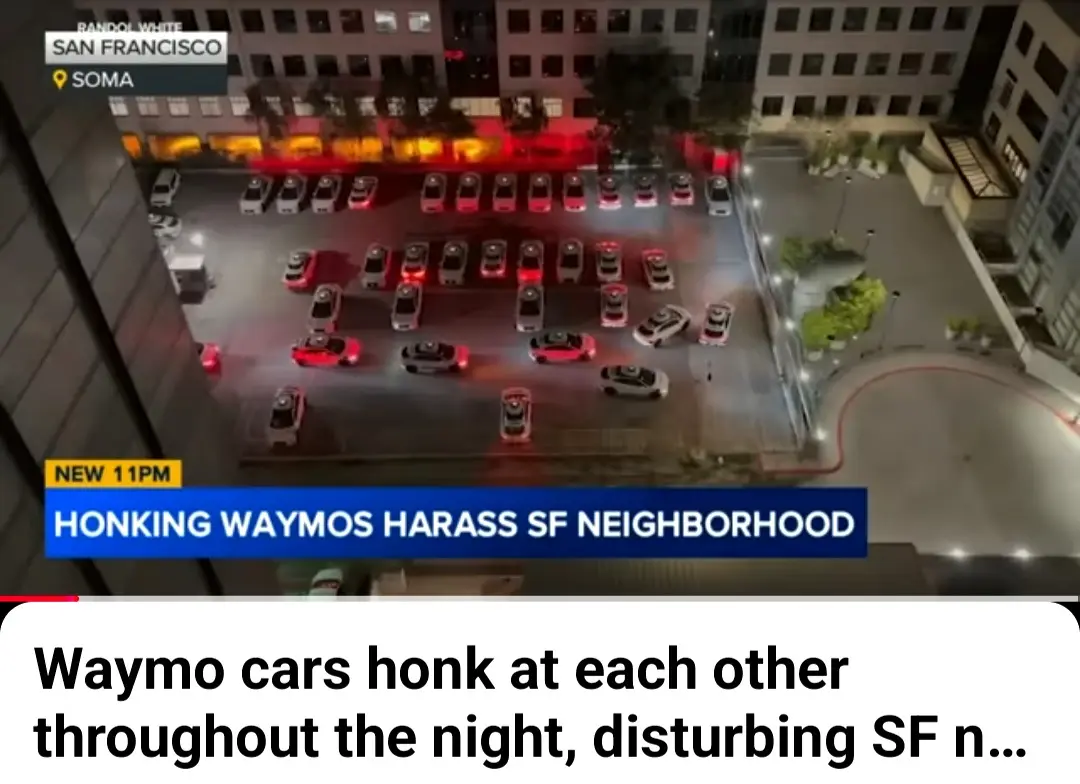 An aerial night view shows dozens of white Waymo self-driving cars parked in a city lot in San Francisco's SOMA district…