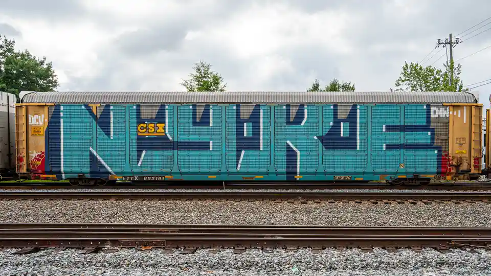 A teal and blue CSX freight train car with large graffiti-style lettering spelling 'NIKE' across its side, parked on…