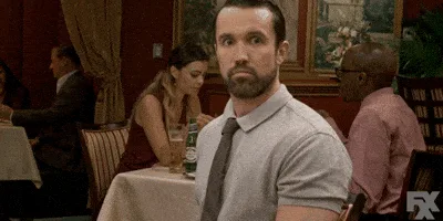A still from the TV show 'It's Always Sunny in Philadelphia' shows a man in a grey polo shirt and tie sitting at a…