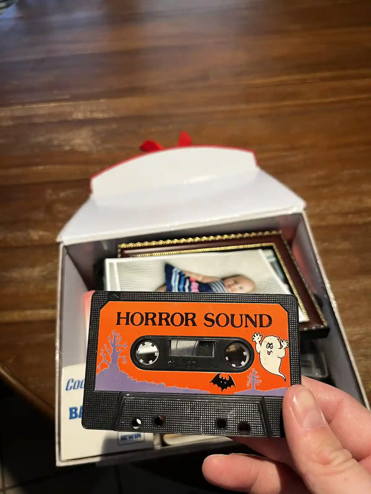 A hand holds a small, decorative cassette tape with an orange label that reads 'HORROR SOUND' and features a cartoon ghost…