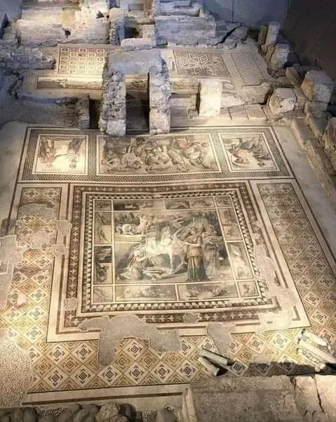 an ancient roman mosaic floor depicts mythological scenes with figures on horseback, surrounded by geometric patterns, with…