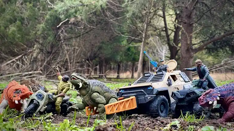 A staged outdoor scene features toy action figures and vehicles, including a green armored vehicle with two figures, one…