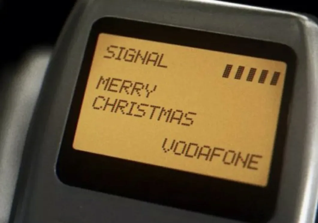 A close-up of an old mobile phone screen displaying a yellowish pixelated message that reads 'SIGNAL ||||', 'MERRY…