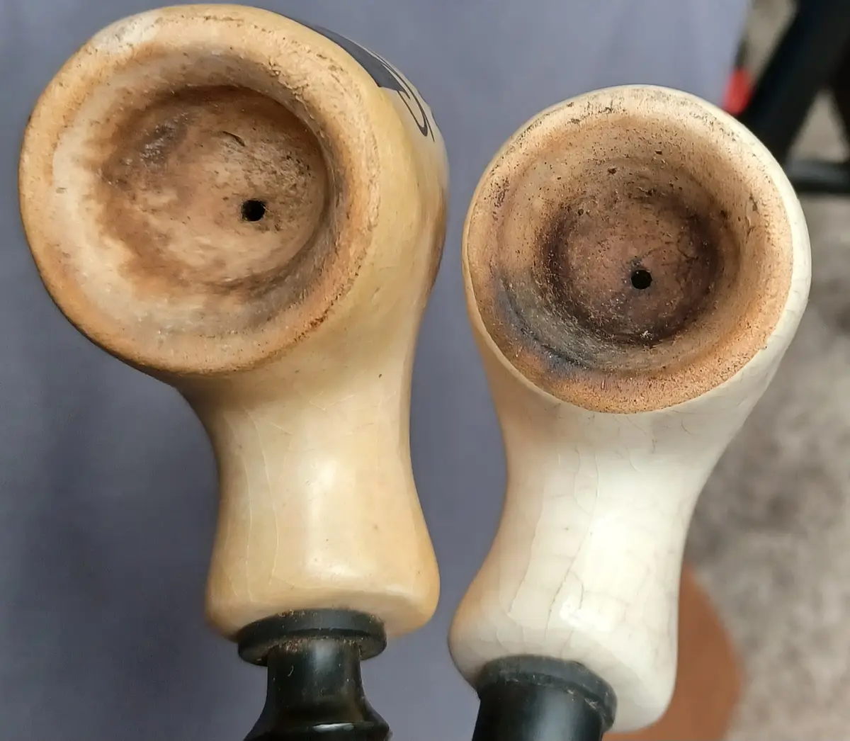 Two vintage-style ceramic pipe bowls are shown side by side, both heavily stained with dark residue and ash inside their…