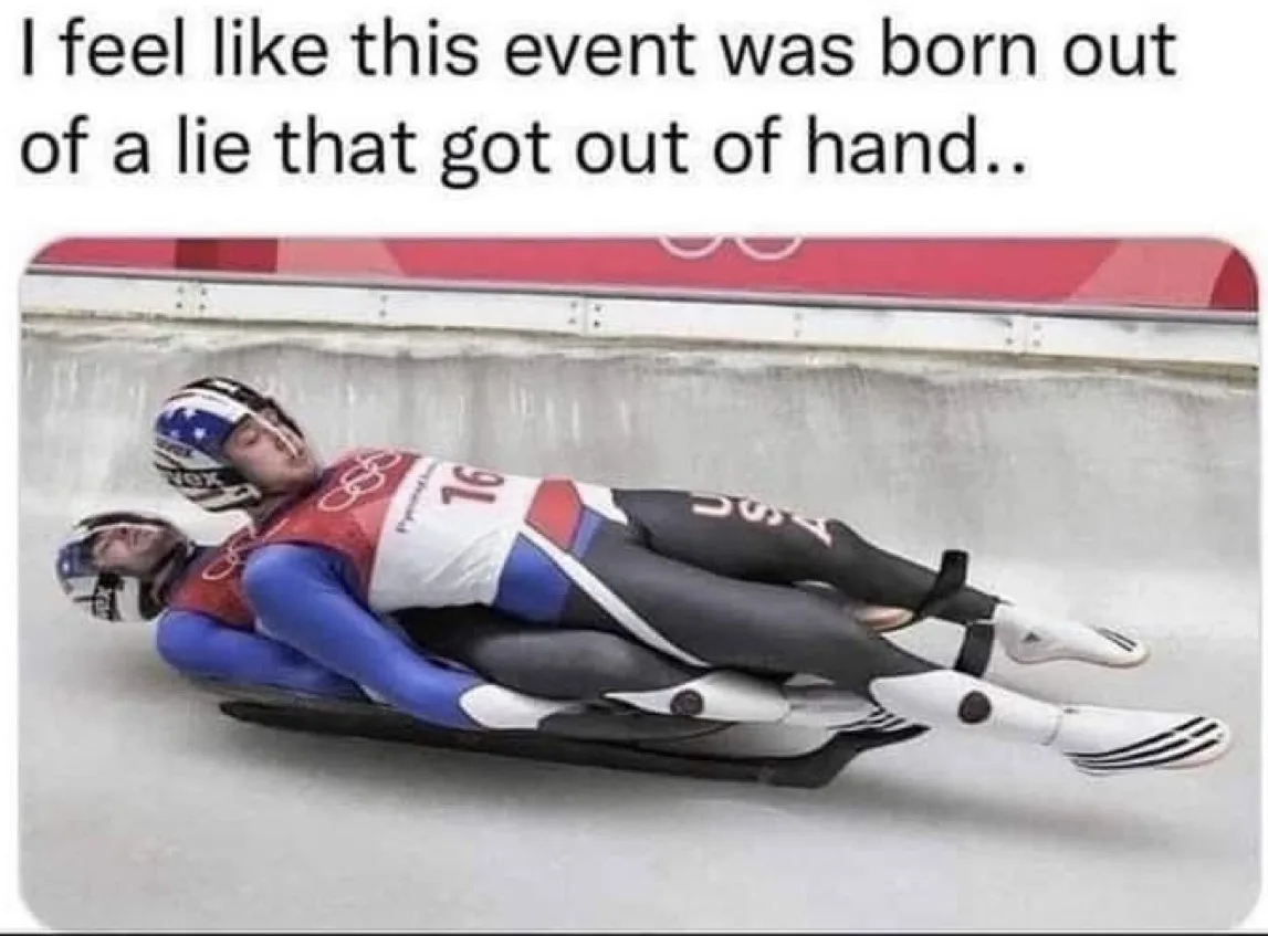 Two athletes in Olympic luge uniforms are lying prone on a sled, appearing to be asleep or exhausted, as they glide down an…
