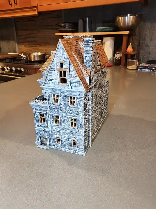 A detailed miniature model of a gothic-style stone castle with brown tiled roofs sits on a modern kitchen countertop…