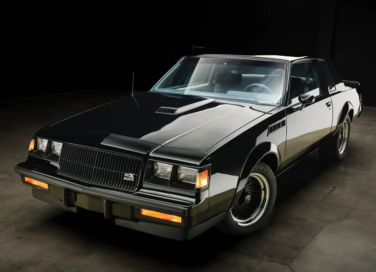 A glossy black and white 1980s Buick Grand National, shown in a studio with dramatic lighting, has the text 'i'm not a car…