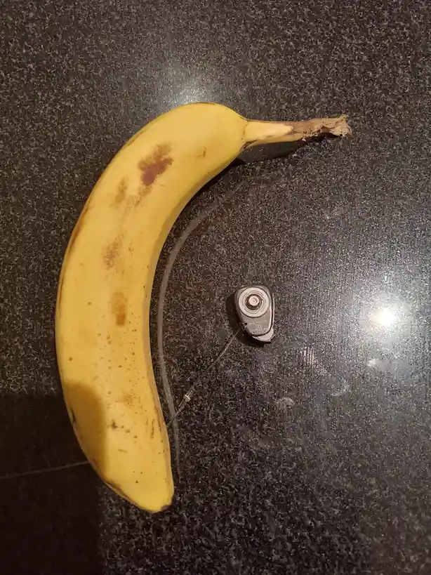 A ripe yellow banana with brown spots lies on a dark speckled countertop, its curved shape forming a crescent moon. Attached…