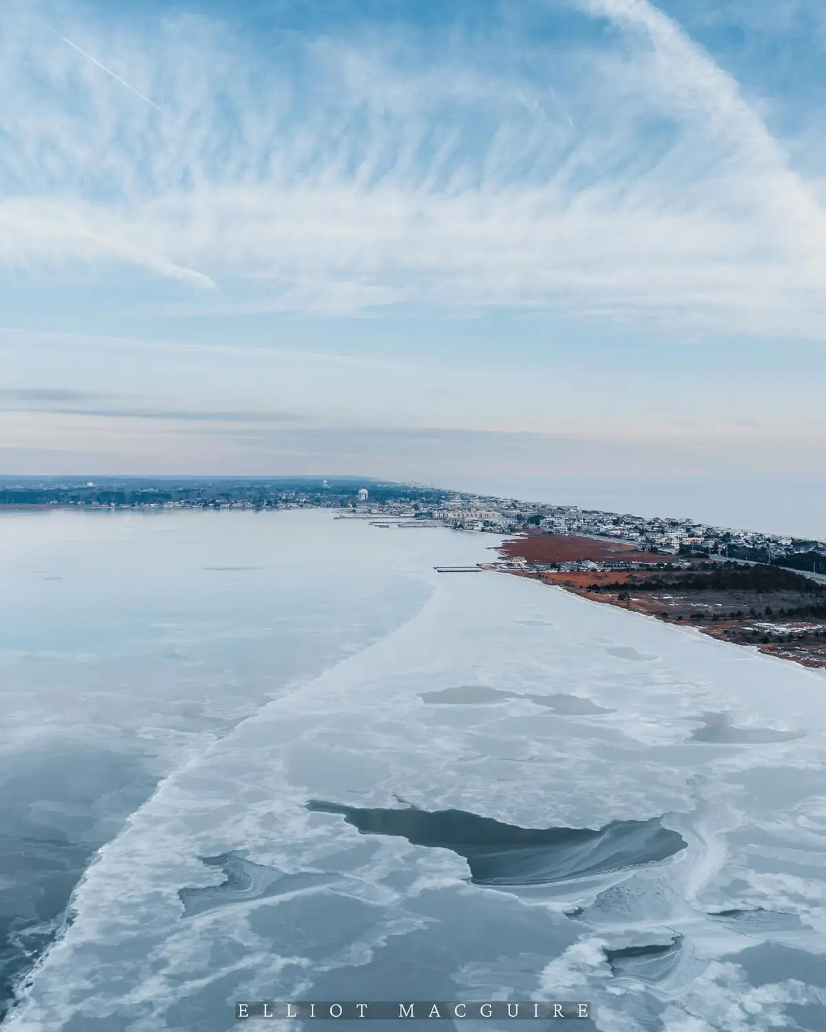 An aerial photograph shows a wide, icy waterway with a distinct, winding line of ice separating a frozen expanse from a…