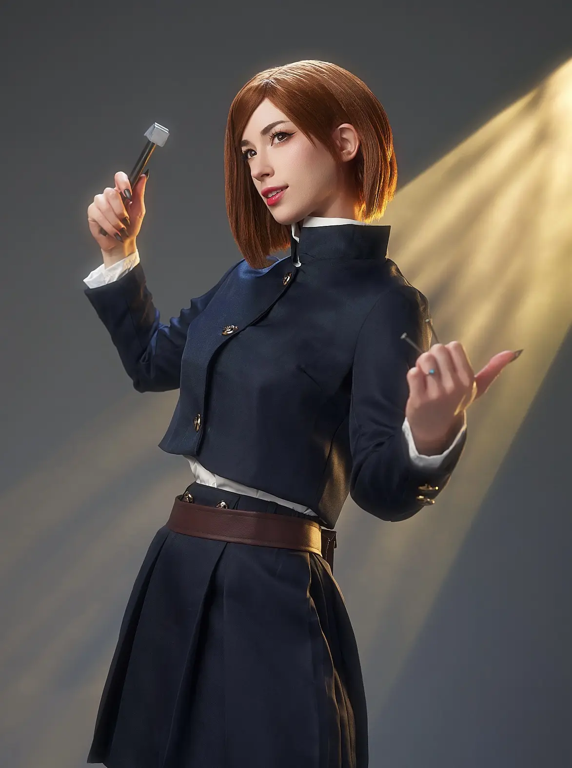 A person in a dark blue school uniform with a white collar and brown belt holds a hammer in one hand and a nail in the…