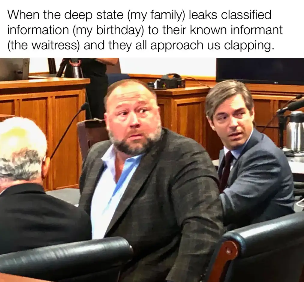 A photo of two men in suits sitting in a courtroom, one with a surprised expression looking up and to the side, the other…